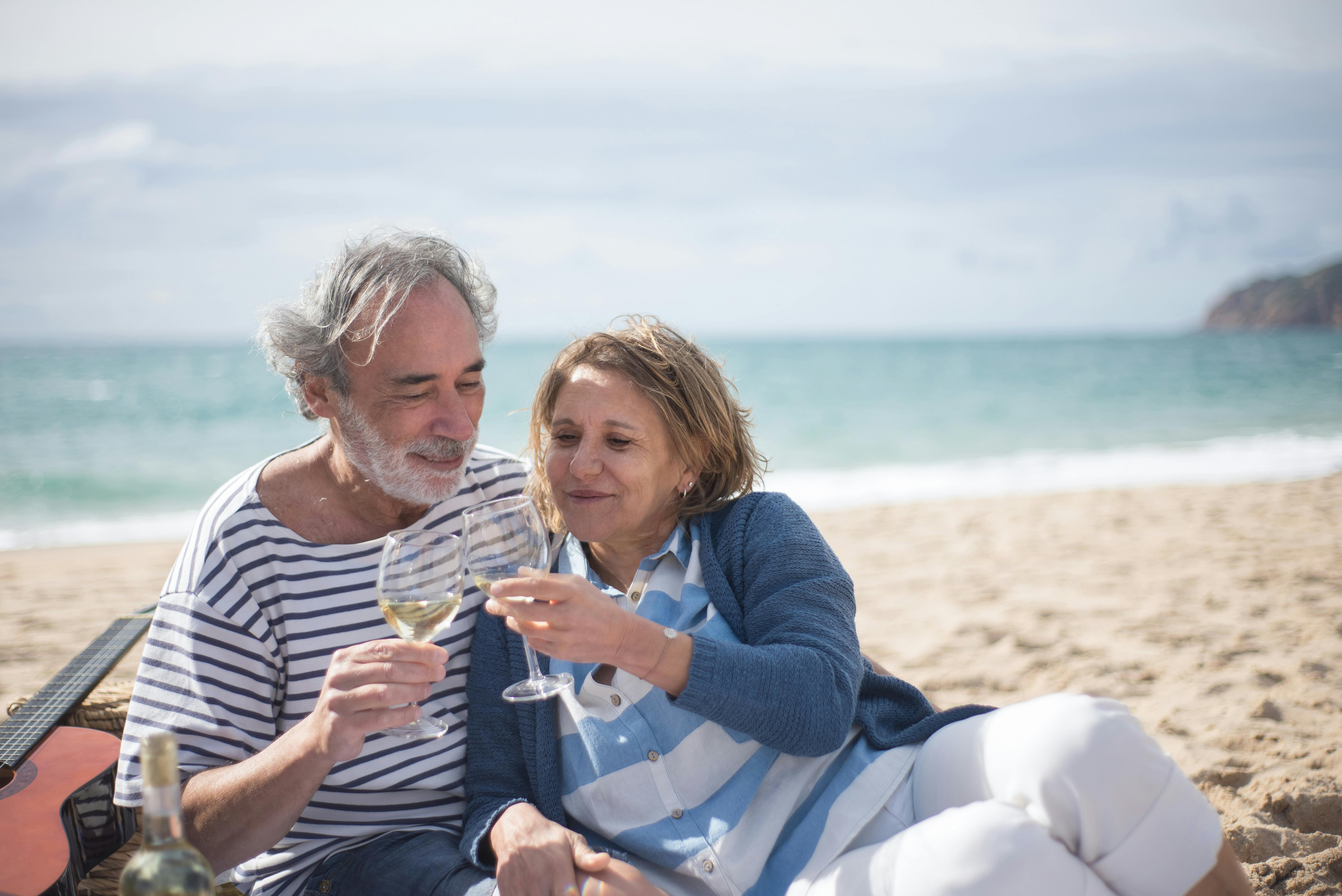 Retired couple toasting wine on a sunlit beach, marking the milestone of reaching Social Security claiming eligibility at age 62