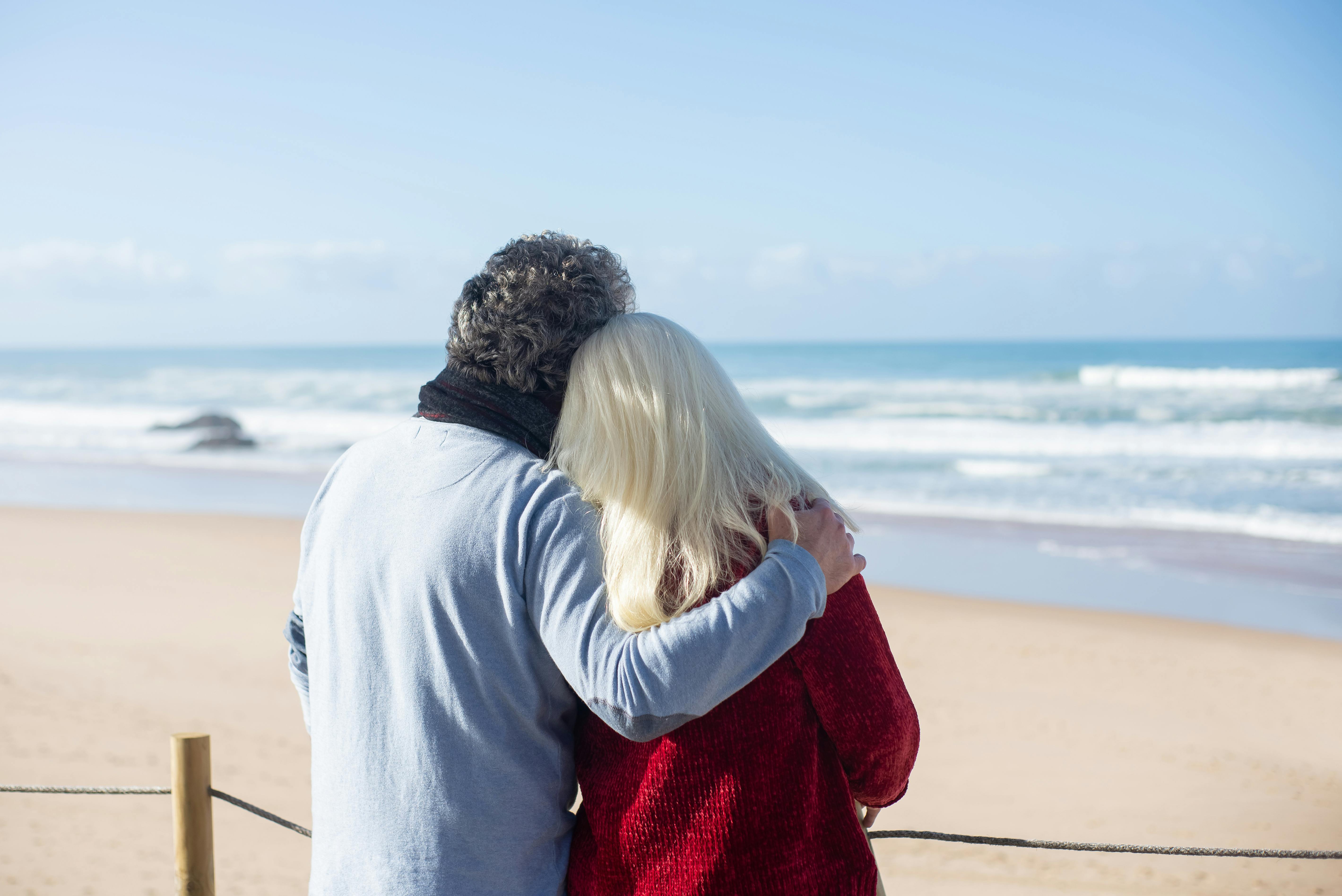 Mature couple embracing on a beach, the emotional weight of the claim-early-or-wait Social Security decision
