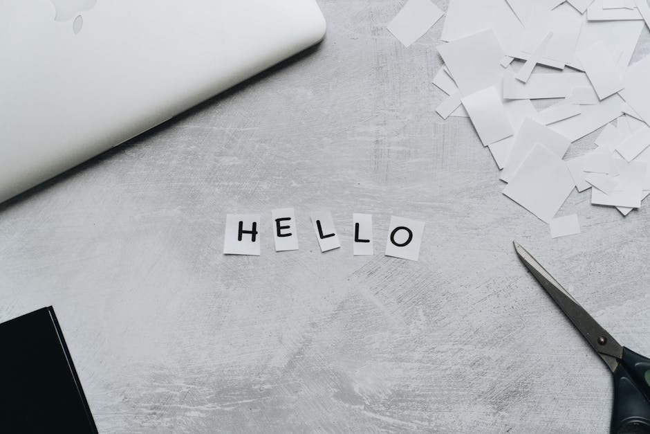 Flat lay of a creative workspace with scissors and cut out letters spelling 'hello' on a textured surface.