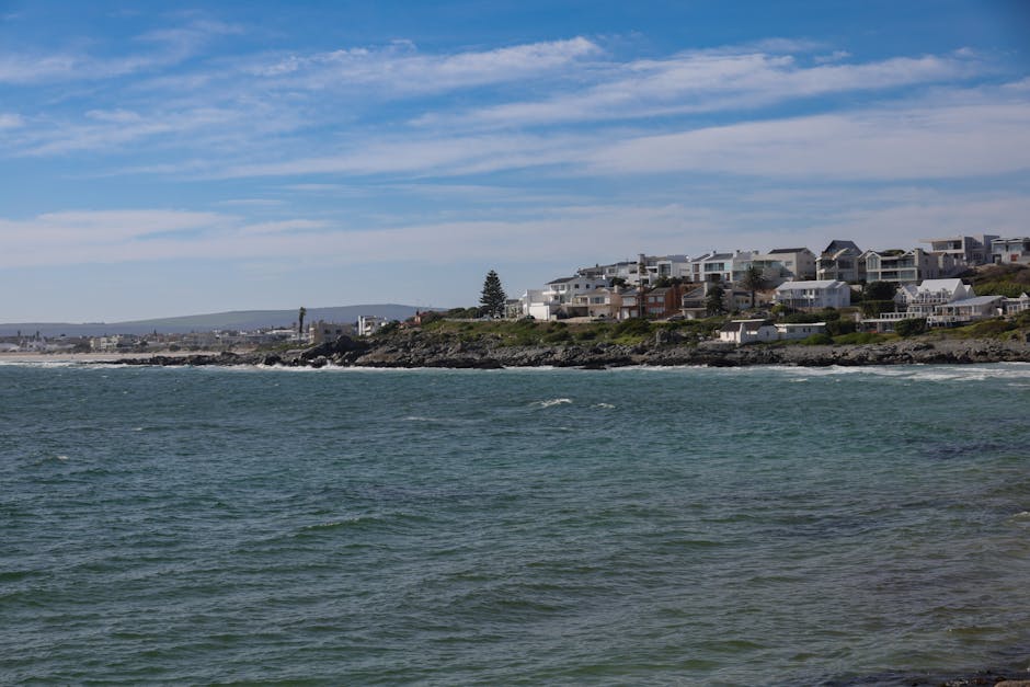 Picturesque coastline with ocean waves and coastal houses under a clear blue sky.